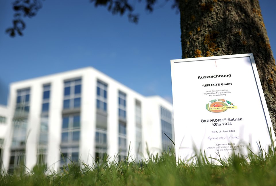 Ökoprofit Köln Urkunde in Rahmen vor Reflects Firmengebäude