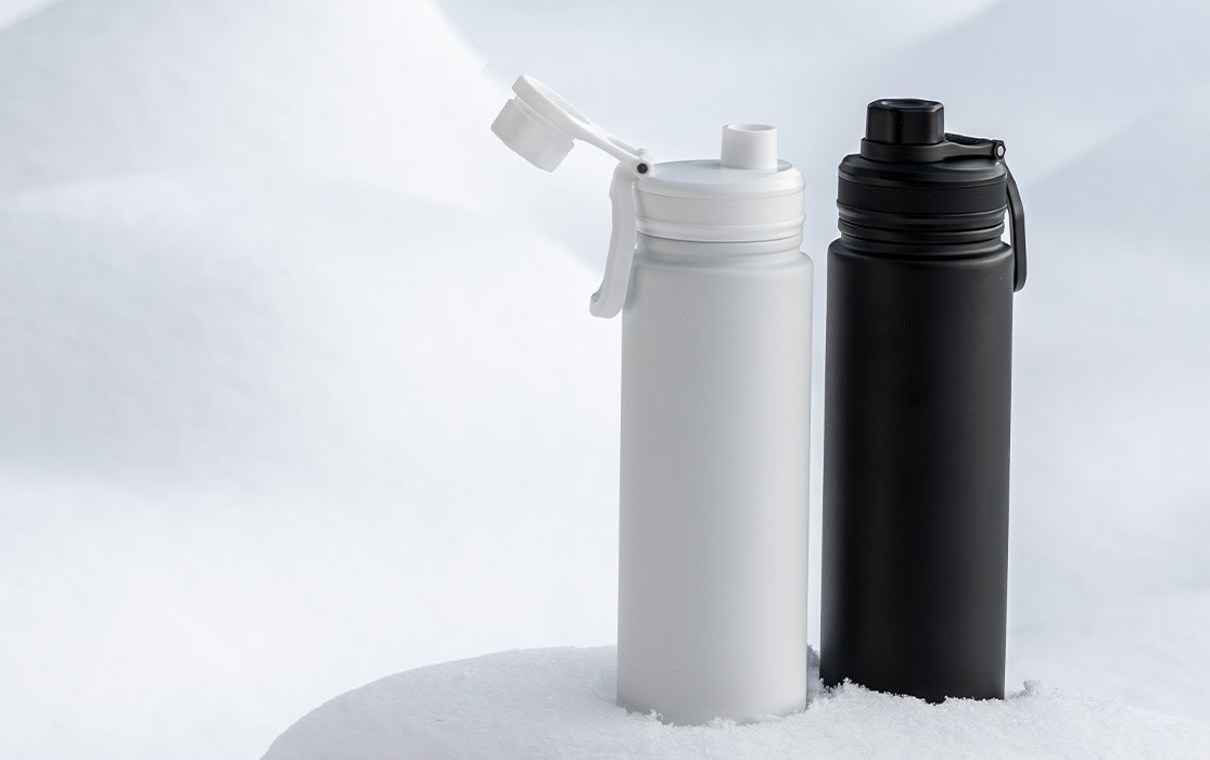 Zwei Thermoflaschen in Schwarz und Weiß stehen im Schnee